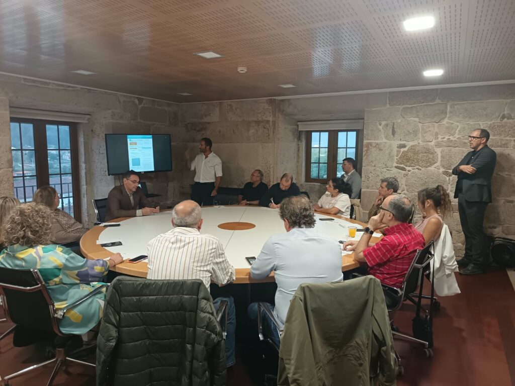 Jornada formativa de RUIZ RE con asistentes reunidos alrededor de una mesa redonda mientras un ponente presenta contenidos en una pantalla.