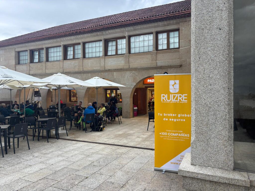 Roll-up de RUIZ RE con el mensaje «Tu broker global de seguros» junto a la entrada de un edificio de piedra con terraza.