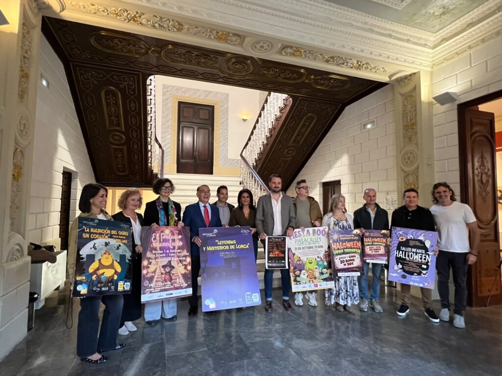 Foto de grupo de los participantes en la presentación de Halloween en Lorca, con los carteles de las actividades, junto a una escalera señorial.